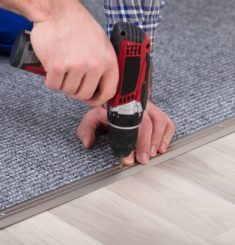 Close-up Of A Carpet Fitter's Hand Installing Grey Carpet With Wireless Screwdriver